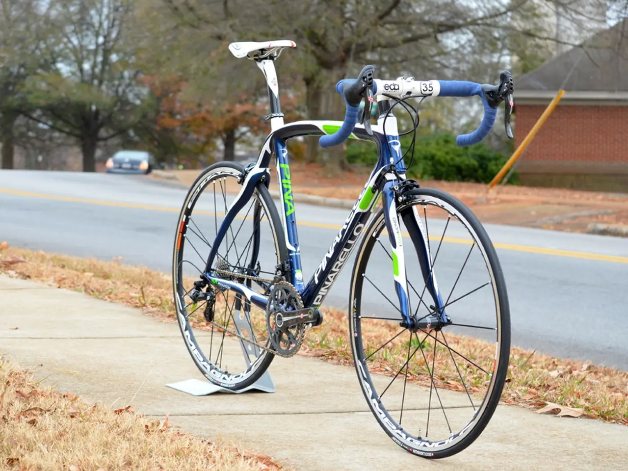 This is a bicycle , on the sidewalk and a house and trees on the side of the road and a car on the...