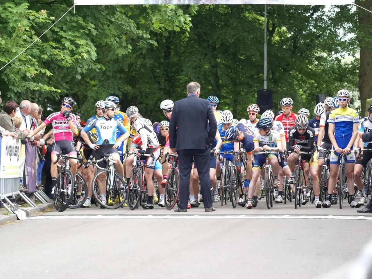 There are group of riders sitting on a bicycle and the person wearing blue suit is standing in...