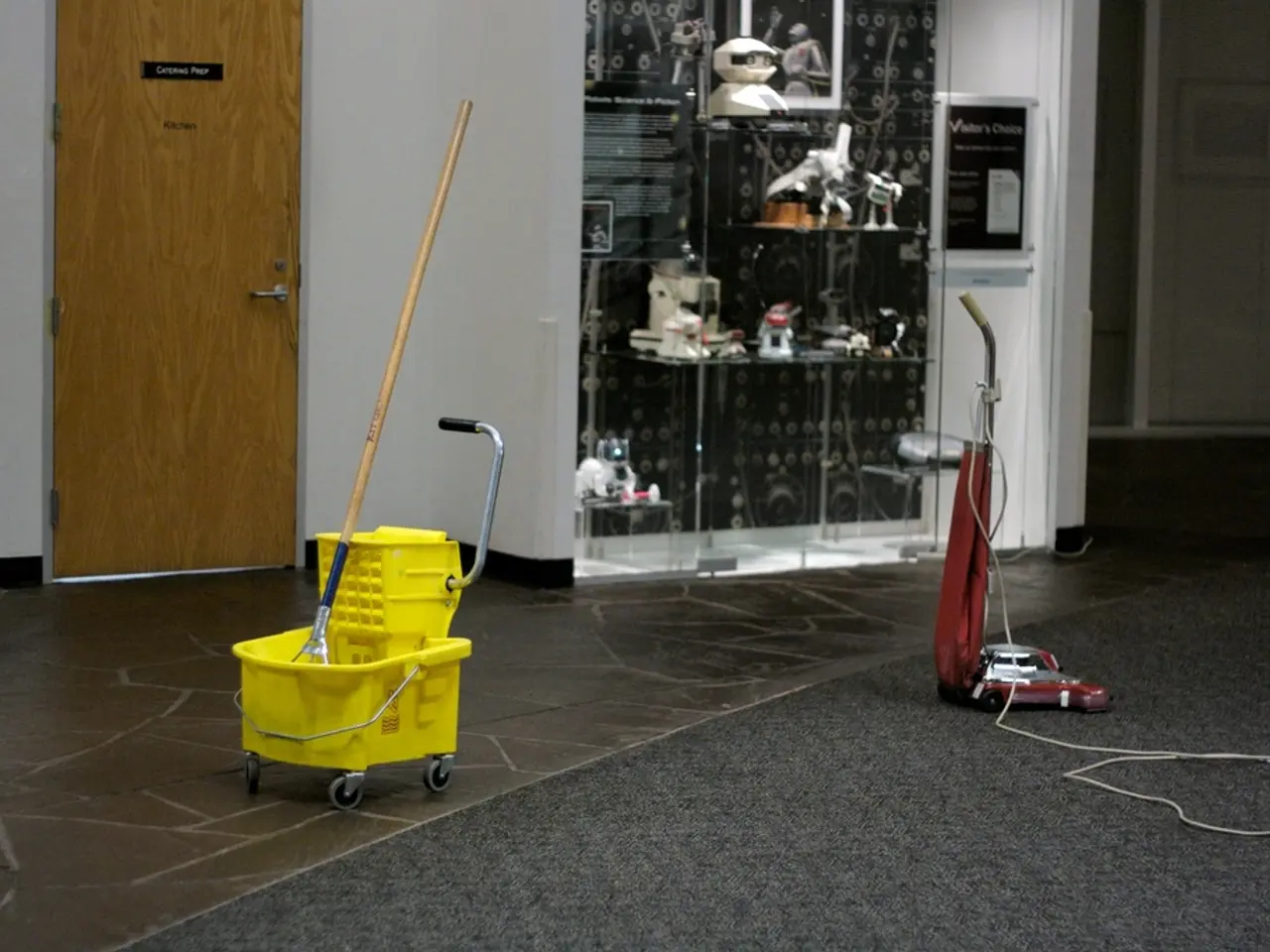 In this image, there is a mop bucket and vacuum cleaner on the floor. There is a rack at the top of...