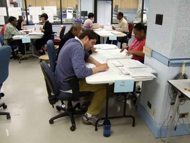 In the picture we can see some people are sitting on a chairs near the desks. They are writing some...