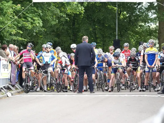 There are group of riders sitting on a bicycle and the person wearing blue suit is standing in...