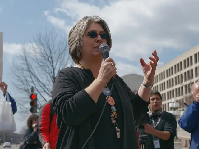 In the image there is a woman holding a microphone for talking, in background there are group of...